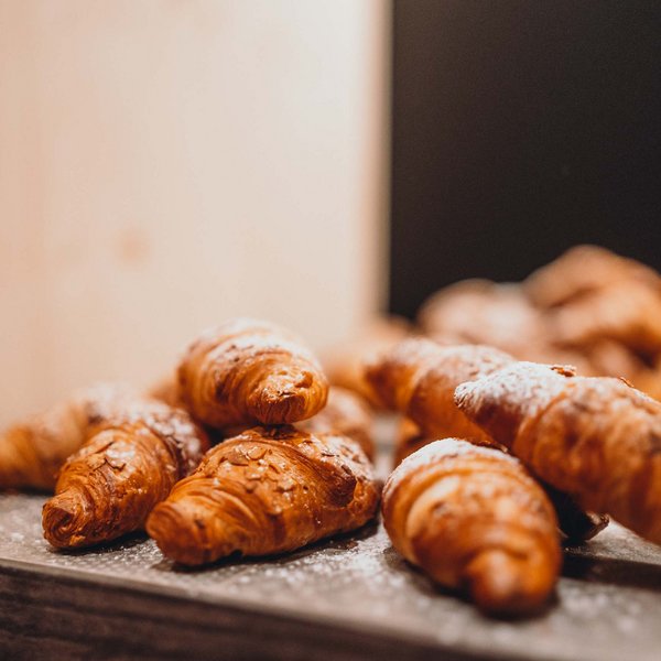 Sensoria Dolomites – Luxury for the Soul Freshly baked croissants dusted with powdered sugar on a dark tray