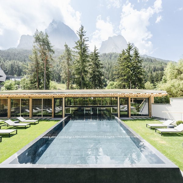 Sensoria Dolomites – Luxury for the Soul Modern pool with lounge chairs and mountain view under cloudy sky