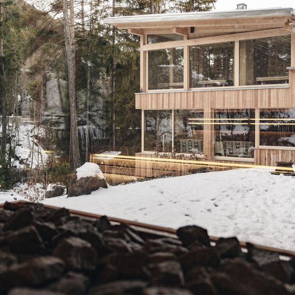 Sensoria Dolomites. Kraftort. Winterzauber. Modernes Holzhaus im Winter mit Schnee und umliegenden Bäumen