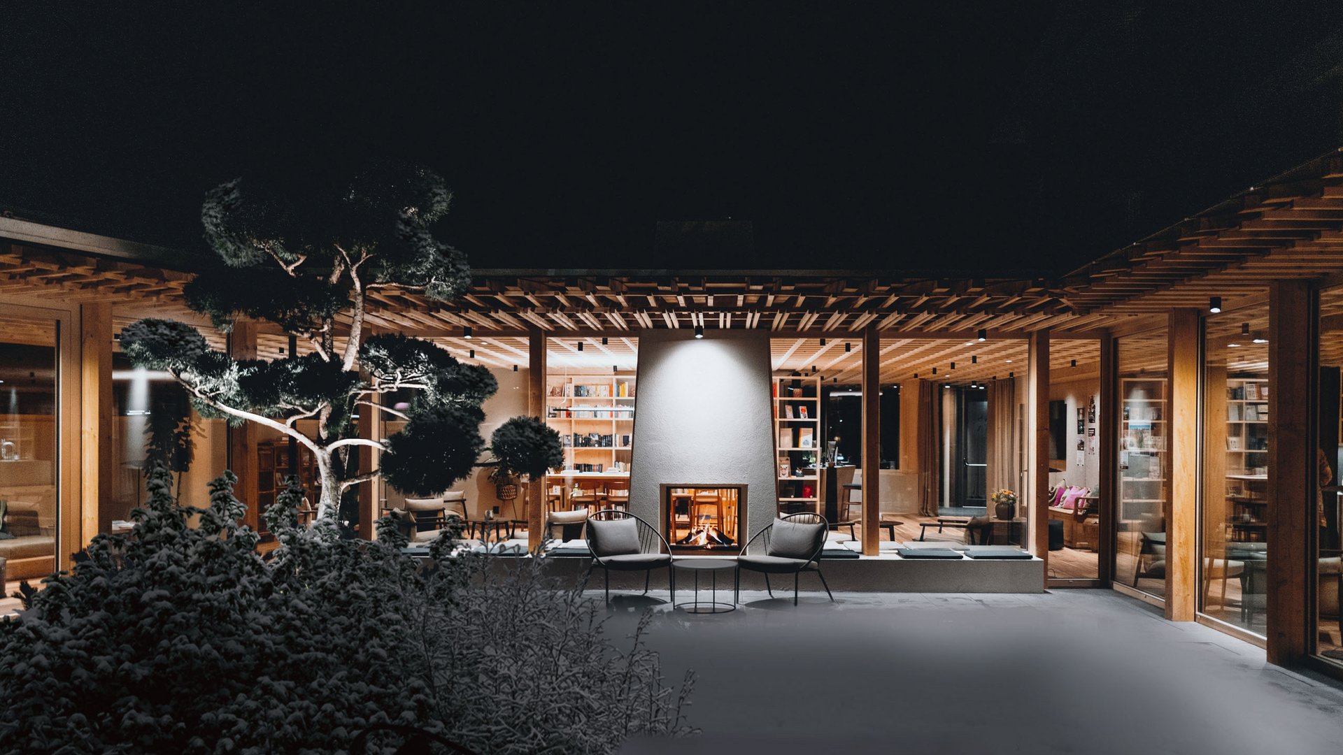 Sensoria Dolomites. Kraftort. Winterzauber. Modernes Haus mit beleuchtetem Innenraum und Kamin bei Nacht