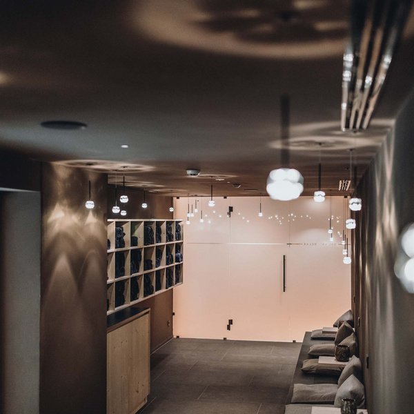 Sensoria Dolomites. Kraftort. Winterzauber. Beleuchteter Spa-Wartebereich mit Hockern und Handtuchregalen