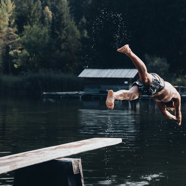 Sensoria Dolomites – Luxury for the Soul A man diving off a diving board into a lake surrounded by forest