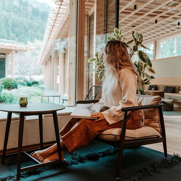 Sensoria Dolomites – Luxury for the Soul Woman sitting in modern room looking out window at green nature