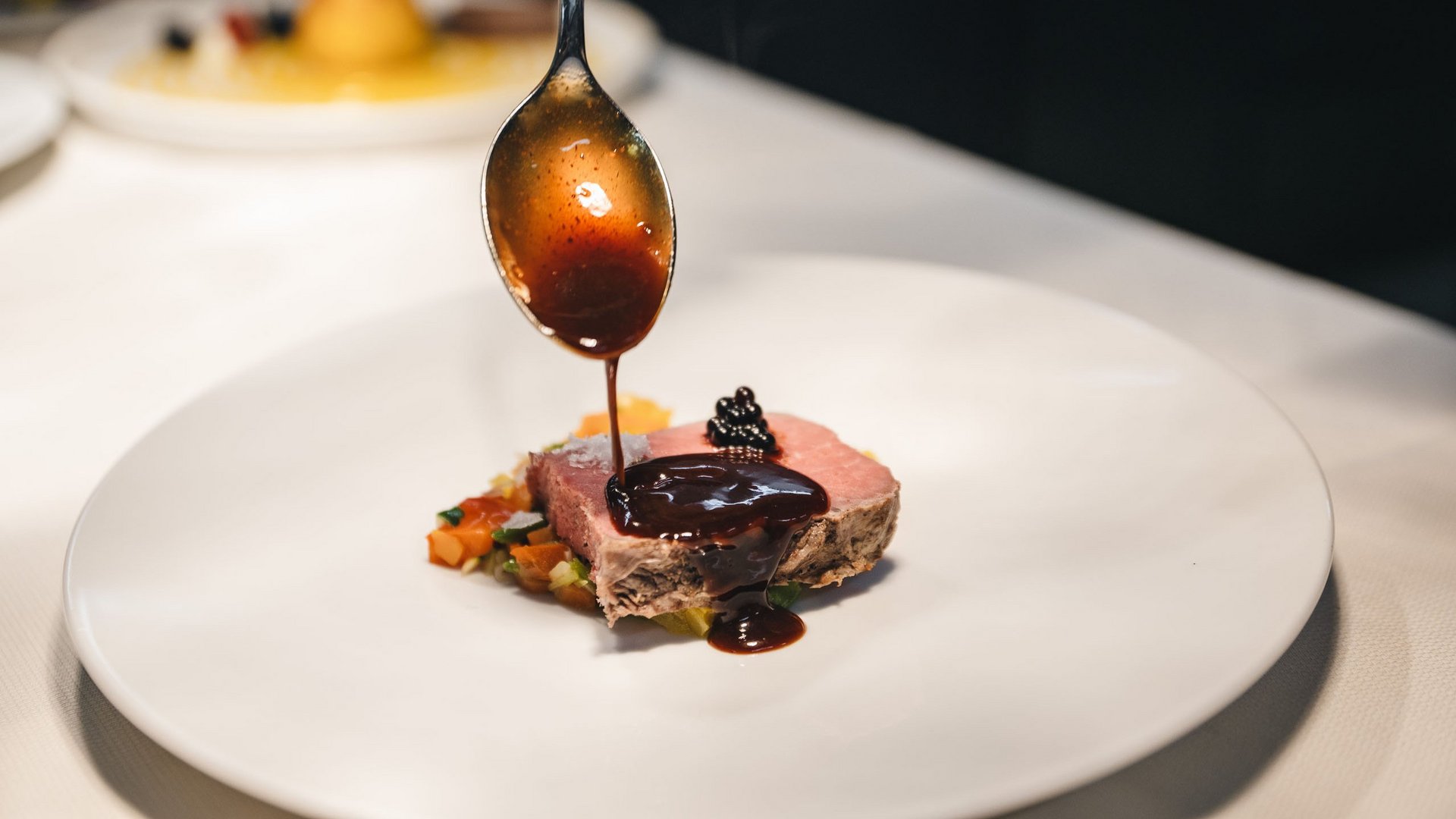 Sensoria Dolomites – Luxury for the Soul Sauce poured from spoon onto slice of meat and vegetables on white plate