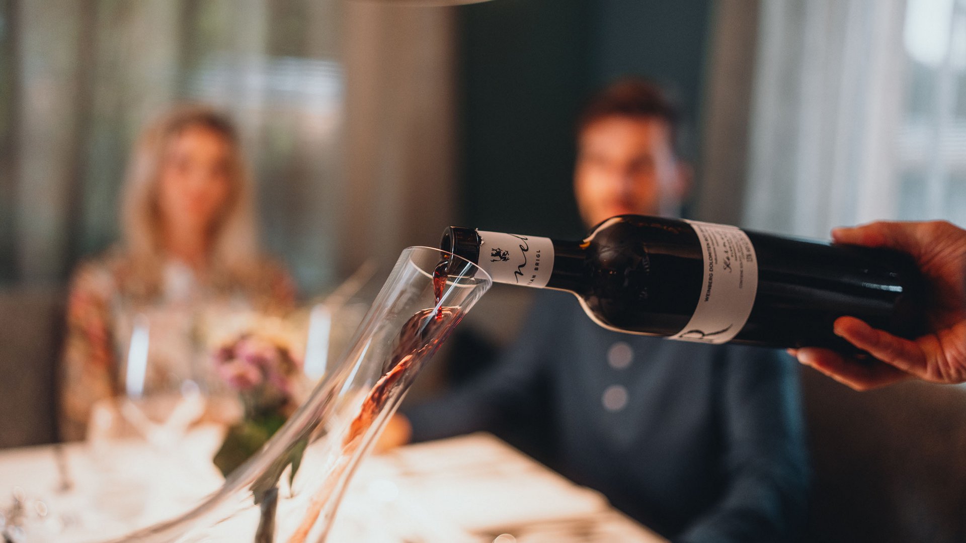 Sensoria Dolomites – Luxury for the Soul Red wine being poured from bottle into decanter at dinner table