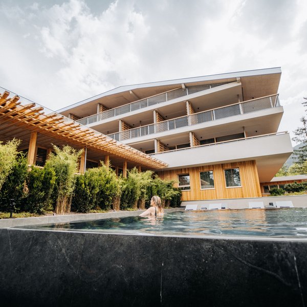 Sensoria Dolomites – Luxury for the Soul Woman relaxing in outdoor pool next to modern hotel building with wooden facade
