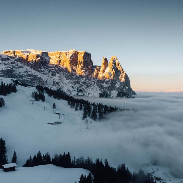 Sensoria Dolomites. Kraftort. Winterzauber. Schneebedeckte Alpenberge mit Sonnenlicht und Wolken im Tal