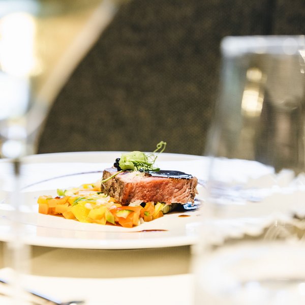 Sensoria Dolomites. Kraftort. Winterzauber. Ein Stück Fleisch mit dunkler Soße und Gemüse auf einem weißen Teller
