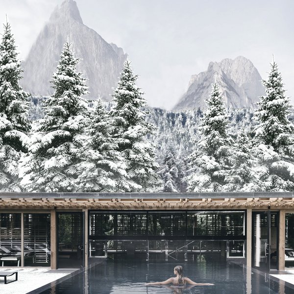 Sensoria Dolomites. Kraftort. Winterzauber. Frau schwimmt im Pool vor verschneiten Bergen und Tannen