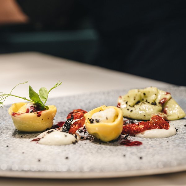 Sensoria Dolomites – Luxury for the Soul Plated tortellini with sauce, dried tomatoes, and herbs on a gray plate