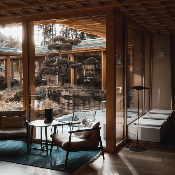 Sensoria Dolomites – Luxury for the Soul Gemütlicher Sitzbereich mit Stühlen und Tisch vor großen Fenstern zum Garten