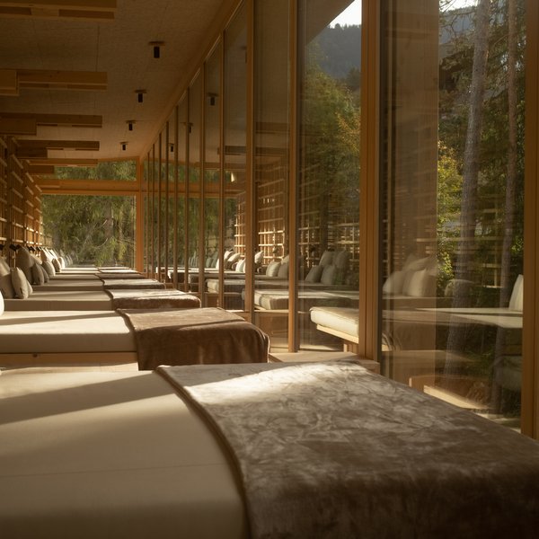 Sensoria Dolomites – Luxury for the Soul Reihe von Liegen mit Kissen und Decken neben großen Fenstern mit Waldsicht