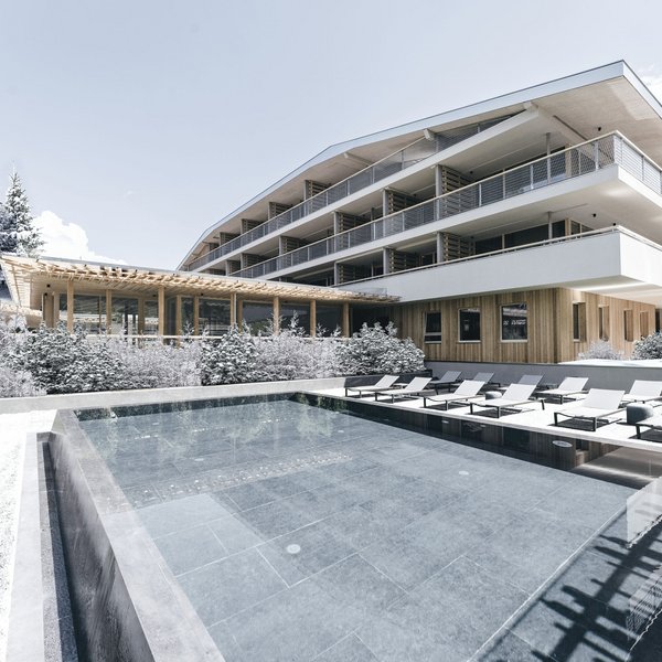 Sensoria Dolomites. Kraftort. Winterzauber. Moderner Hotelkomplex mit Außenpool und Liegestühlen im Winter