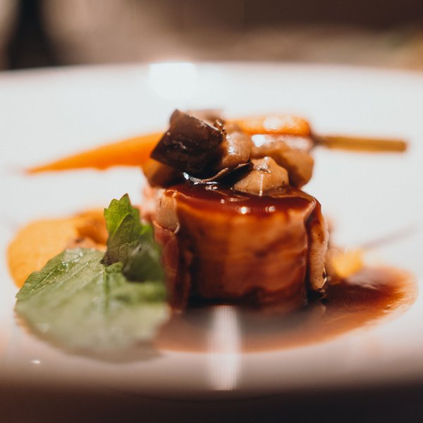 Sensoria Dolomites. Kraftort. Winterzauber. Fein angerichtetes Gourmetgericht mit Sauce, Pilzen und grünem Blatt auf weißem Teller