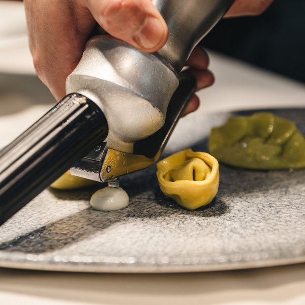 Sensoria Dolomites – Luxury for the Soul Hand applying sauce with a dispenser on stuffed pasta on a plate