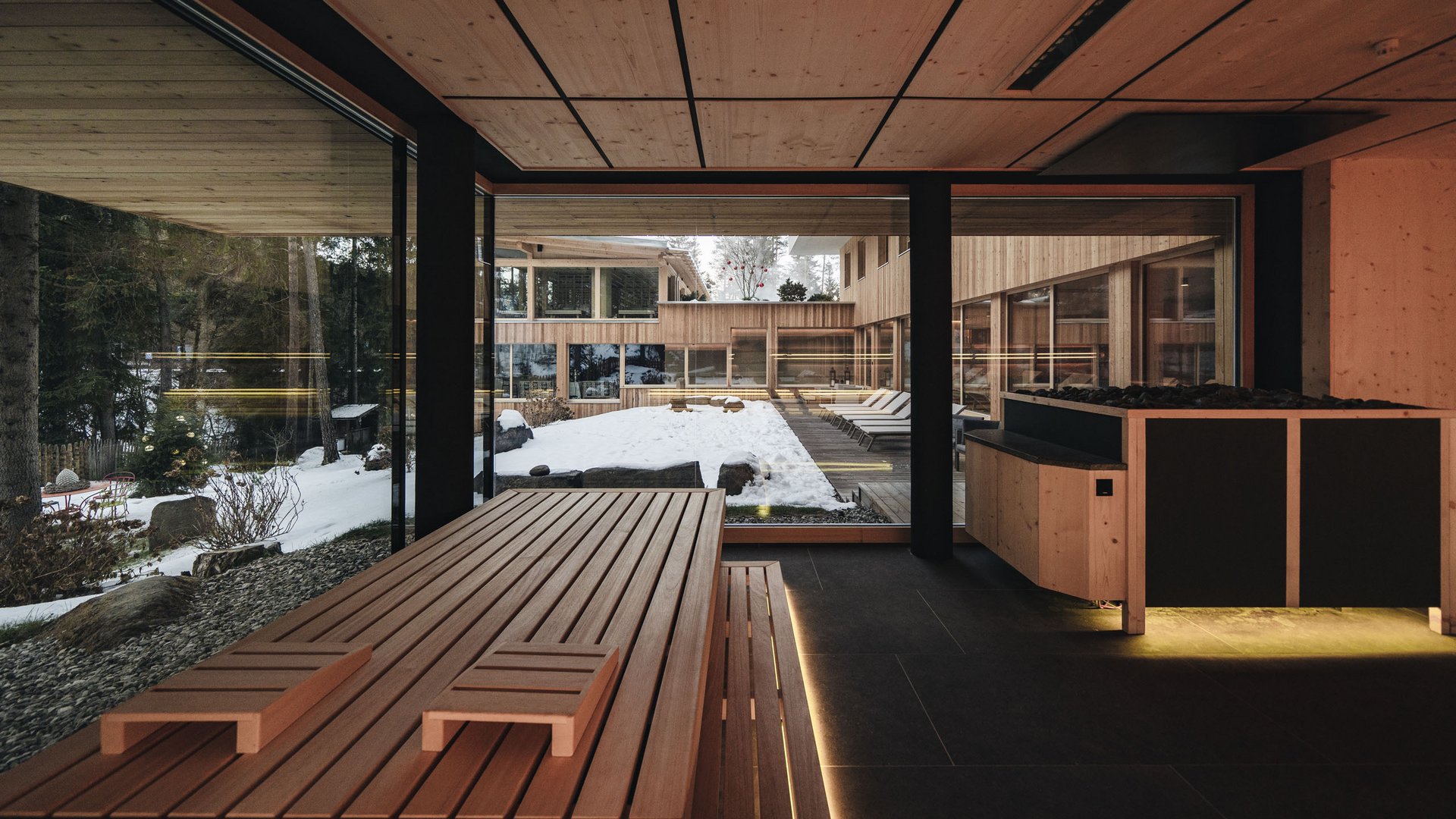 Sensoria Dolomites. Kraftort. Winterzauber. Moderner Sauneraum mit Blick auf verschneiten Außenbereich und Liegestühle