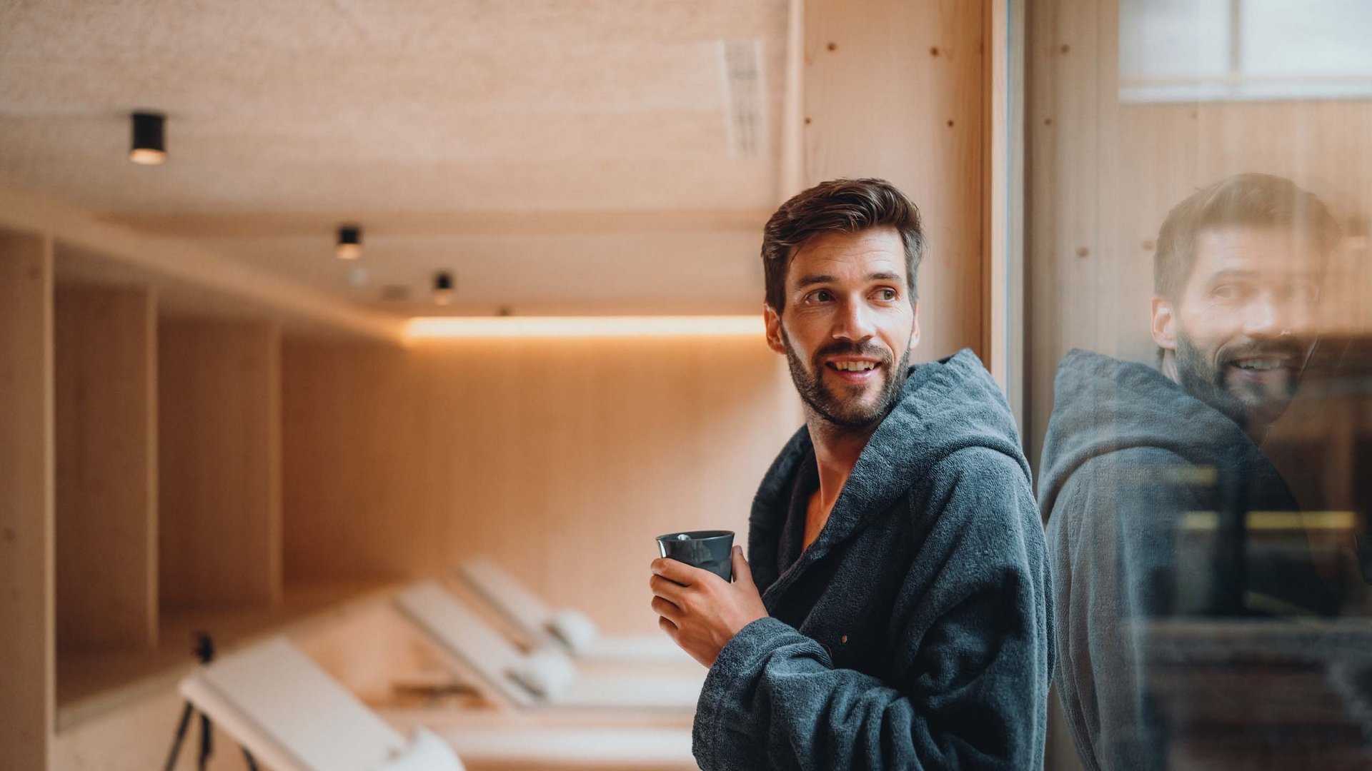 Sensoria Dolomites. Kraftort. Winterzauber. Mann im Bademantel trinkt Kaffee in einem Ruhebereich mit Liegestühlen