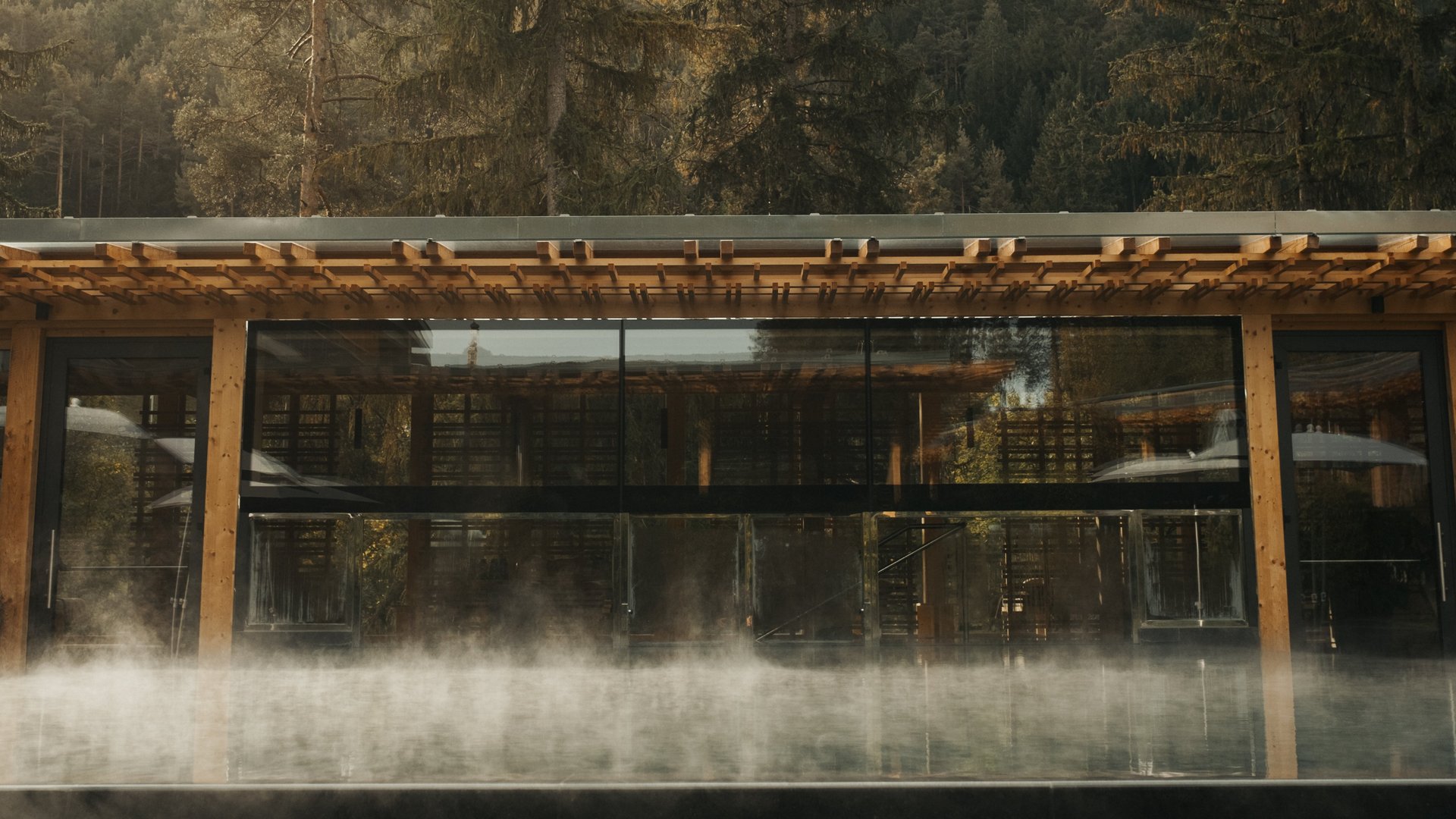 Sensoria Dolomites – Luxury for the Soul Dampfender Außenpool vor Holzgebäude mit Berg und Wald im Hintergrund