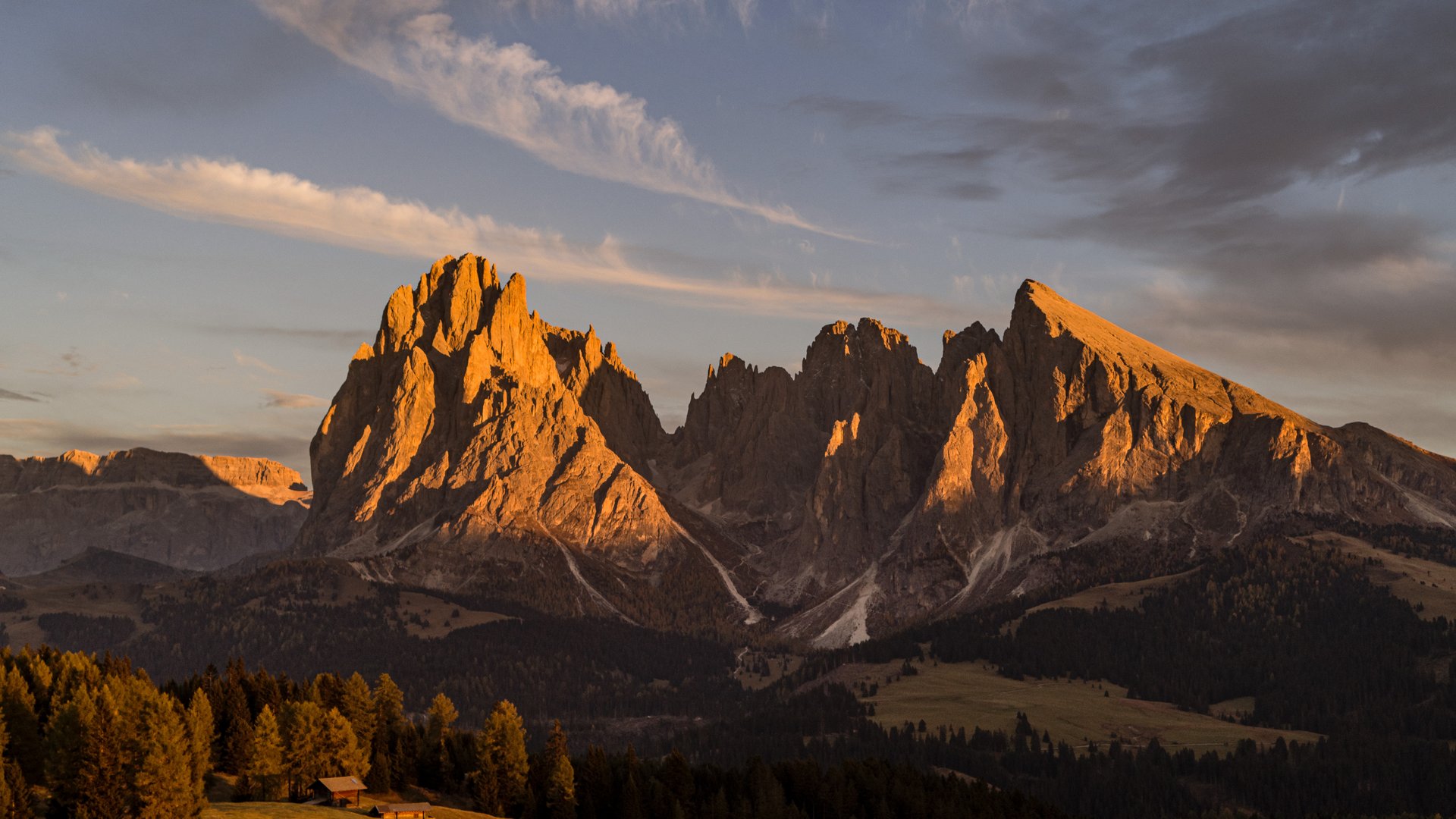 Sensoria Dolomites – Luxury for the Soul Berglandschaft mit Sonnenuntergang über bewaldeten Hügeln und Felsen