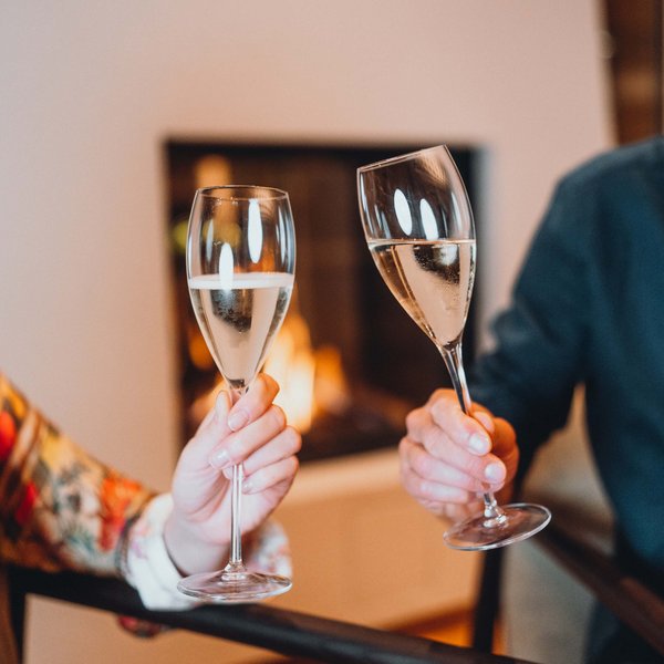 Sensoria Dolomites – Luxury for the Soul Two people clinking champagne glasses in front of a fireplace