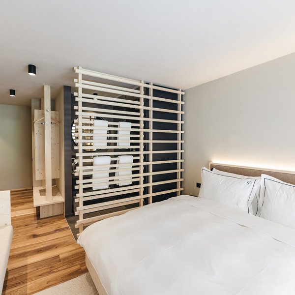Sensoria Dolomites. Kraftort. Winterzauber. Modernes Hotelzimmer mit großem Bett und Holzwandtrenner