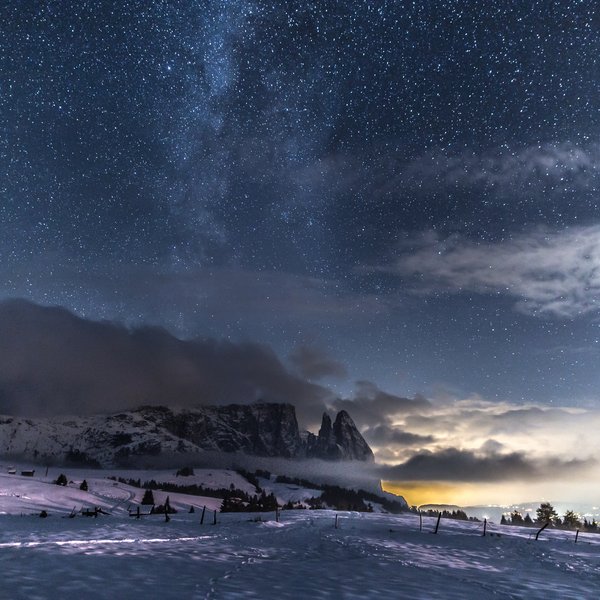 Sensoria Dolomites. Kraftort. Winterzauber. Sternklarer Nachthimmel über schneebedeckten Bergen und Nebel im Tal