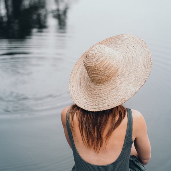Sensoria Dolomites – Luxury for the Soul Woman in straw hat looking at calm water with gentle ripples