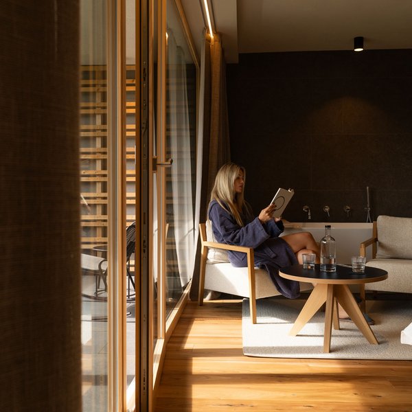 Sensoria Dolomites – Luxury for the Soul Woman in robe reading a book in a modern living room with wooden floor