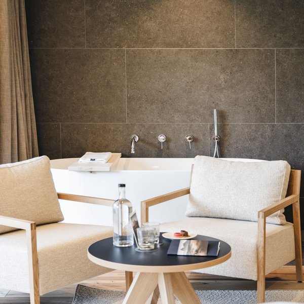 Sensoria Dolomites. Kraftort. Winterzauber. Zwei beige Stühle vor einer Badewanne mit dunkler Wand